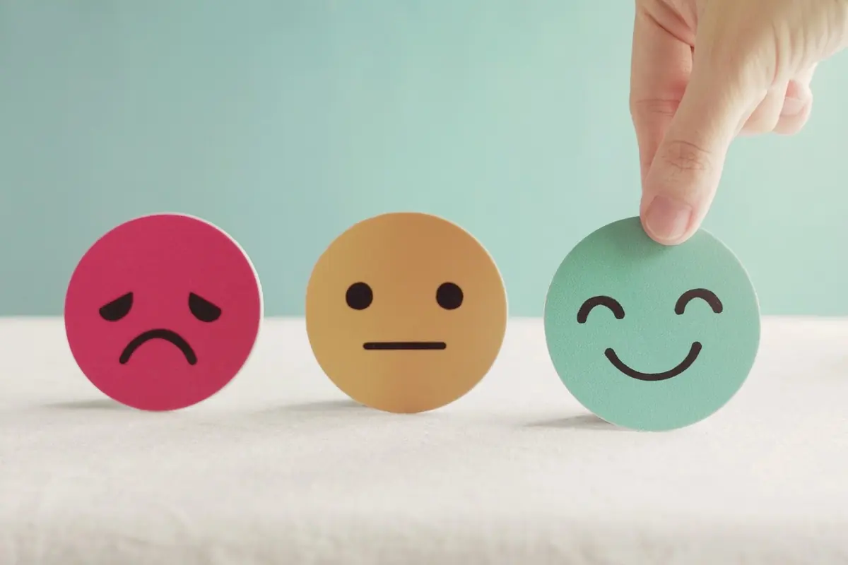 Hand choosing a smiling face from three emotion icons