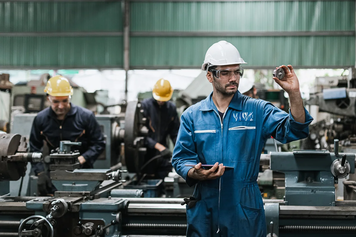 Engineer with a tablet on a factory floor beside machine operators